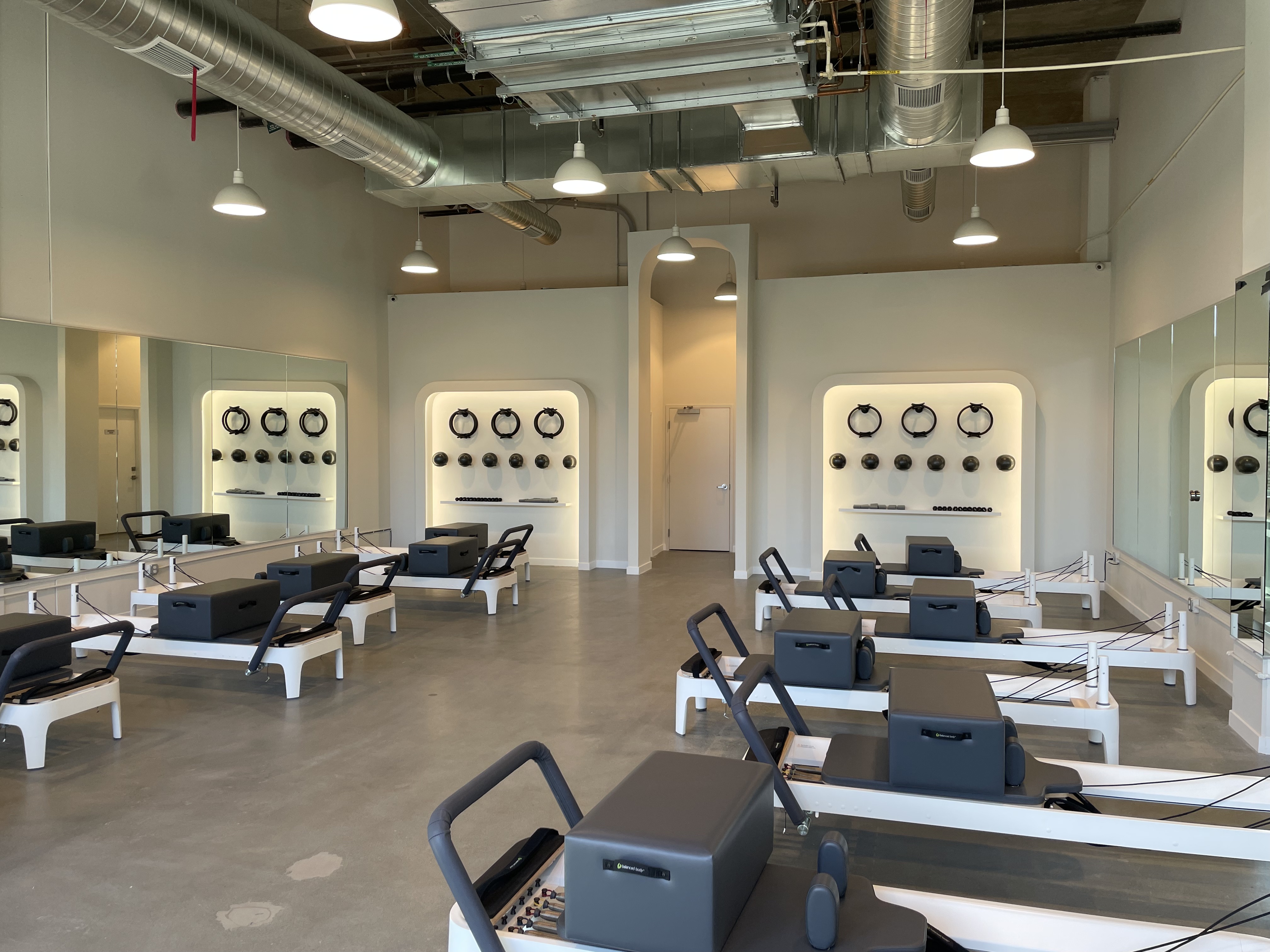 Interior view of a modern pilates studio featuring several reformers, mirrors, and fitness equipment mounted on the walls.